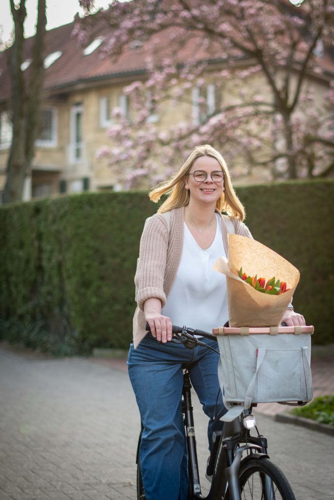 Geraldine Henneböhl auf dem Fahrrad Geraldine Henneböhl, Bürgermeisterkandidatin für Havixbeck und Hohenholte fährt auf ihrem Fahrrad durch Havixbeck. Im Fahrradkorb liegen frische Tulpen vom Markt. Im Hintergrund blühen die Kirschblüten.